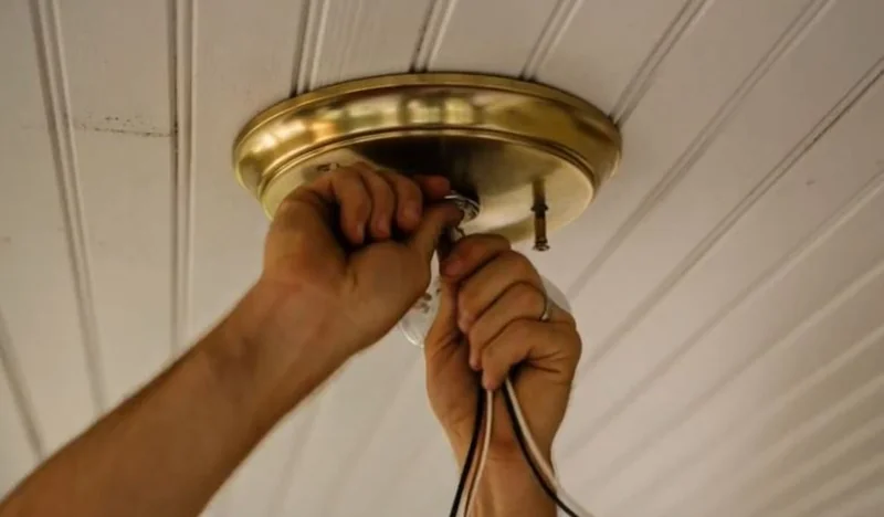 Hands installing a ceiling light fixture on a beadboard ceiling